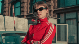 A person wearing sunglasses and a red outfit sitting confidently at an outdoor café table, symbolizing work on the sound design for Kleo Season 2.